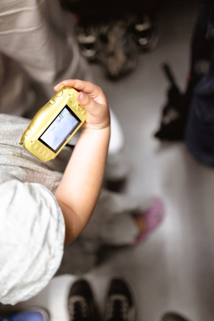 A childs hand holding a yellow digital camera in a crowded space.